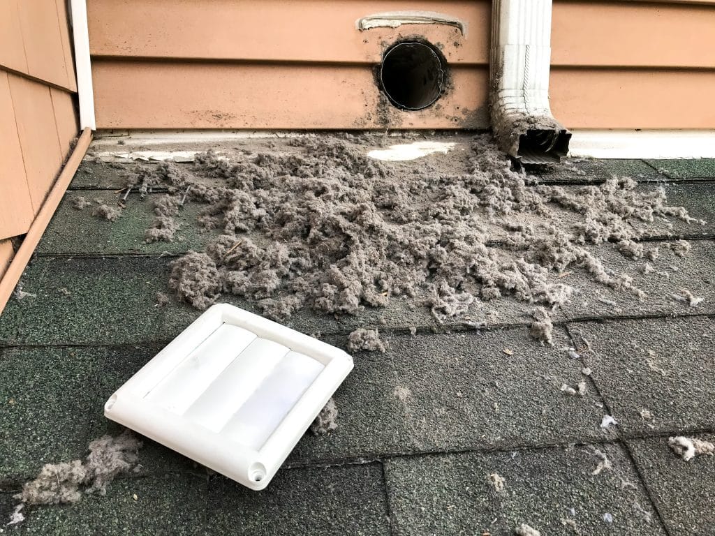 Dirty dryer vent on a roof surrounded by a large buildup of lint and debris, with the vent cover removed.